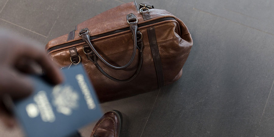 close up view of a person's hand holding a passport and a brown leather duffel bag on the floor